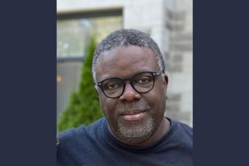 A Black man wearing spectacles, pictured outdoors by a tree